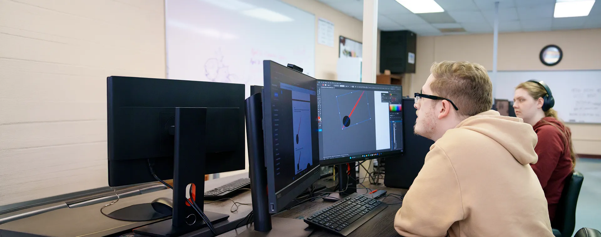 Students work at computer stations displaying CAD software in a classroom with multiple monitors.