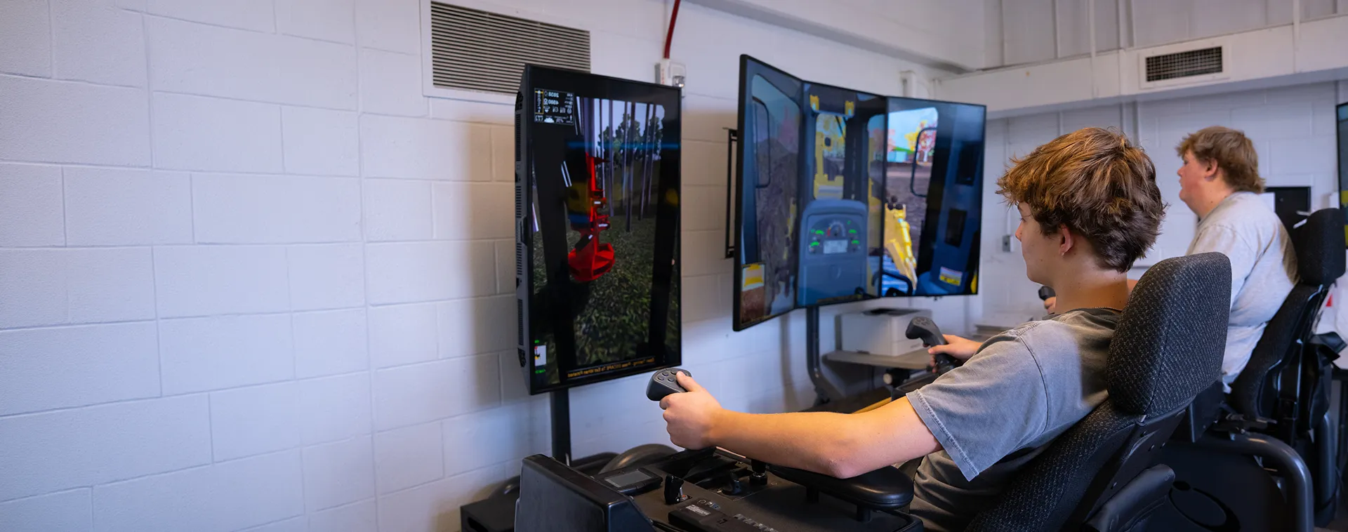 Students operate forestry equipment simulators with large display screens showing heavy machinery controls.