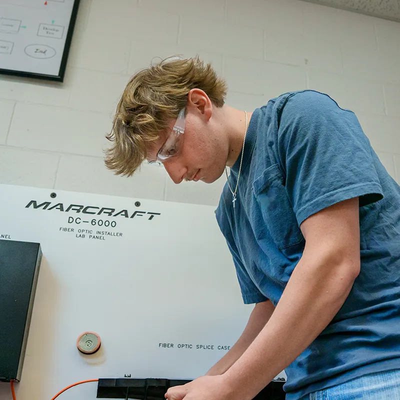Student wearing safety glasses working at a fiber optic installer lab panel
