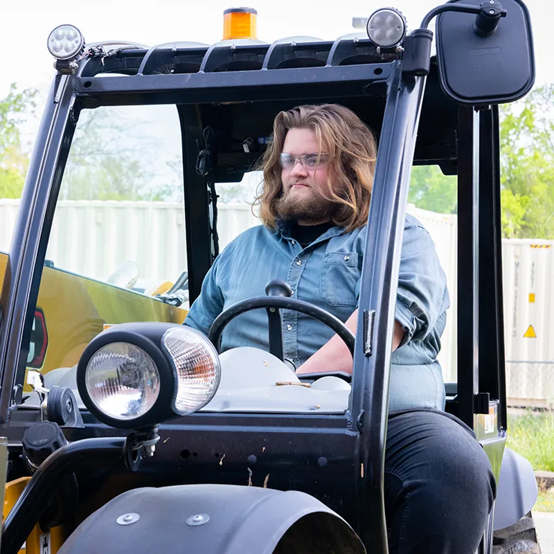 Student wearing safety glasses operates a forklift outdoors.