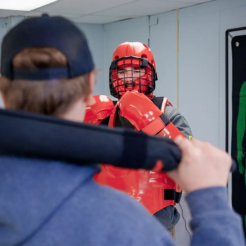 Close view of a defensive tactics training exercise with protective gear and a padded training baton.
