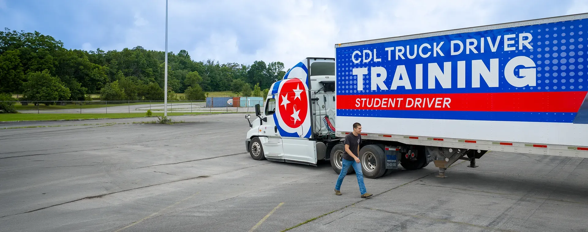 CDL training truck parked in a paved lot with a student walking beside the trailer marked &ldquo;CDL Truck Driver Training.&rdquo;