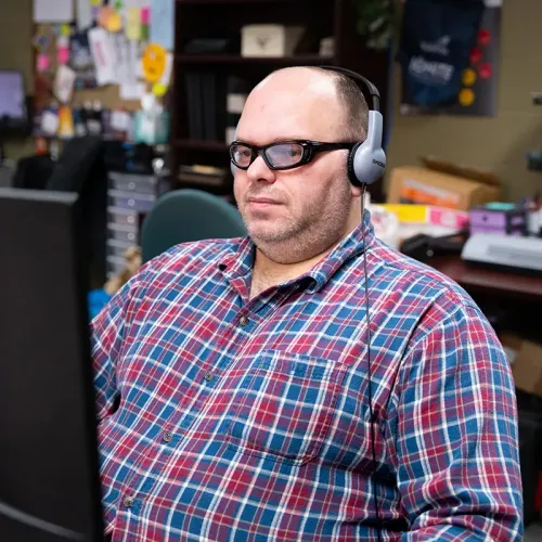 Person wearing headphones and glasses seated at a computer workstation in an office.