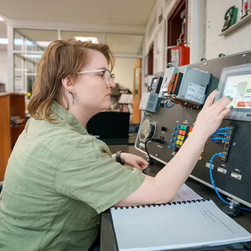 Student uses a touchscreen interface on an industrial control training panel with wiring and control modules.