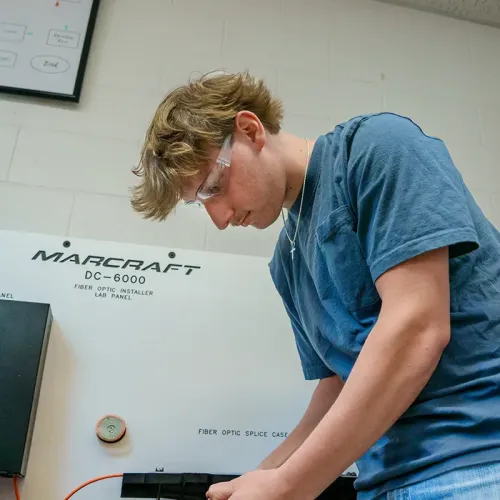 Student wearing safety glasses working at a fiber optic installer lab panel
