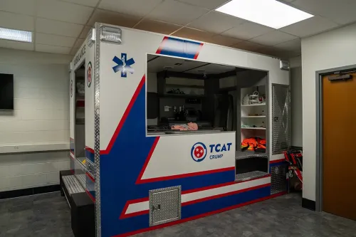 Ambulance training simulator inside a classroom with open storage compartments and medical equipment.