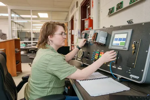 Student adjusts controls and wiring on an industrial automation training panel with a touchscreen display.