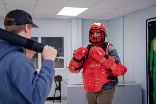 Two people participate in a defensive tactics training exercise, with one wearing red protective equipment.