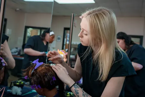 Student styles hair on a mannequin head with sectioning clips at a salon workstation.