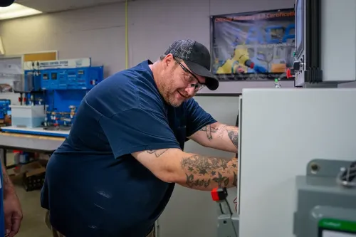 Student adjusts components inside an industrial maintenance training machine in a workshop.