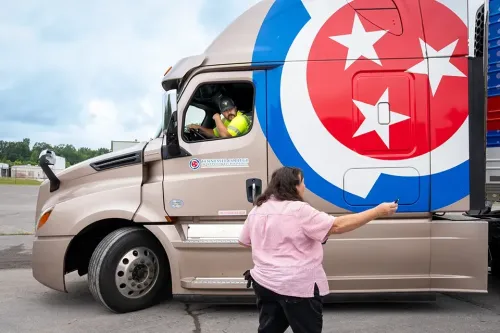Person standing beside a CDL training truck while another person sits in the cab during a vehicle inspection exercise.